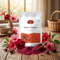 A stand-up pouch of Nature's Basket Hibiscus Powder on a solid beige background. The packaging is primarily white with a coral-orange block at the bottom containing a black hibiscus flower illustration.