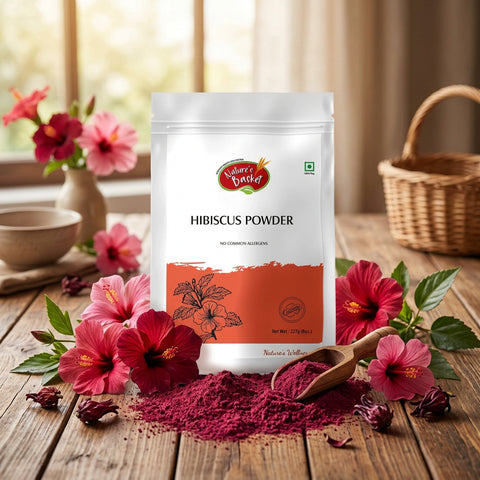 A stand-up pouch of Nature's Basket Hibiscus Powder on a solid beige background. The packaging is primarily white with a coral-orange block at the bottom containing a black hibiscus flower illustration.